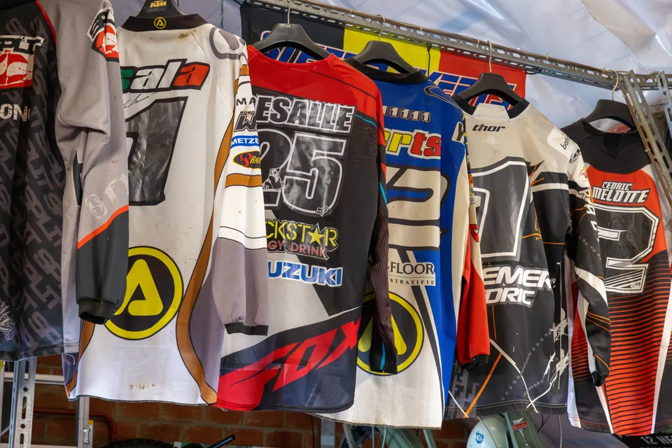 Des maillots de moto colorés sont suspendus côte à côte dans le garage d’Olivier.