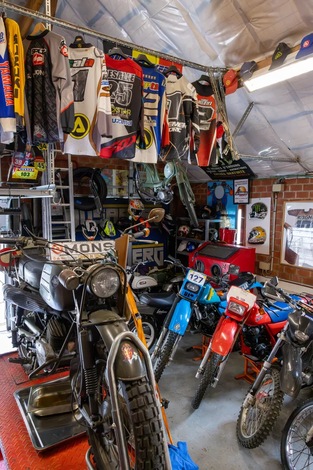 Plusieurs motos sont rangées dans le garage d’Olivier, sous une rangée de maillots de moto.