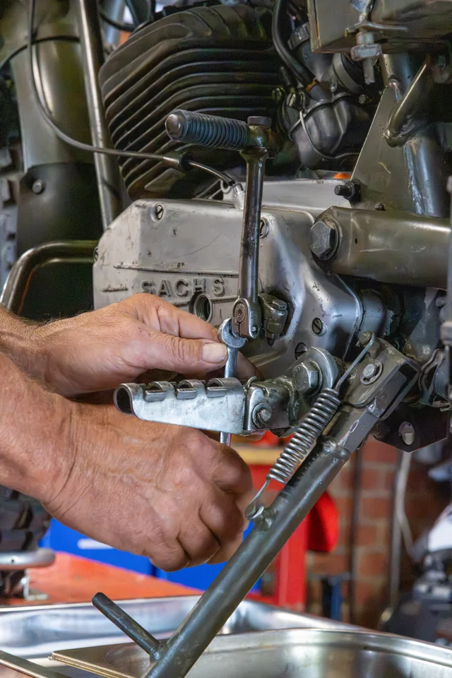 Gros plan sur les mains d’Olivier travaillant près du carter d’un moteur de moto ancienne.