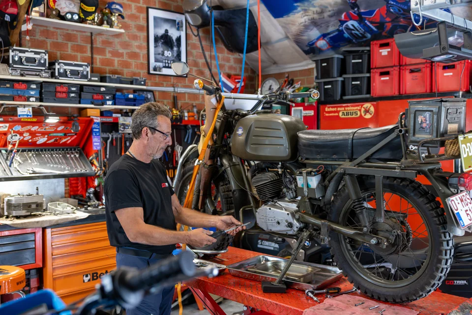 Olivier intervient sur une moto ancienne posée sur un pont rouge, au milieu de son atelier.
