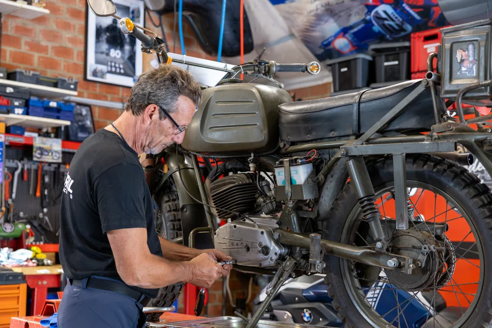Olivier travaille sur le moteur d’une moto ancienne dans son atelier.