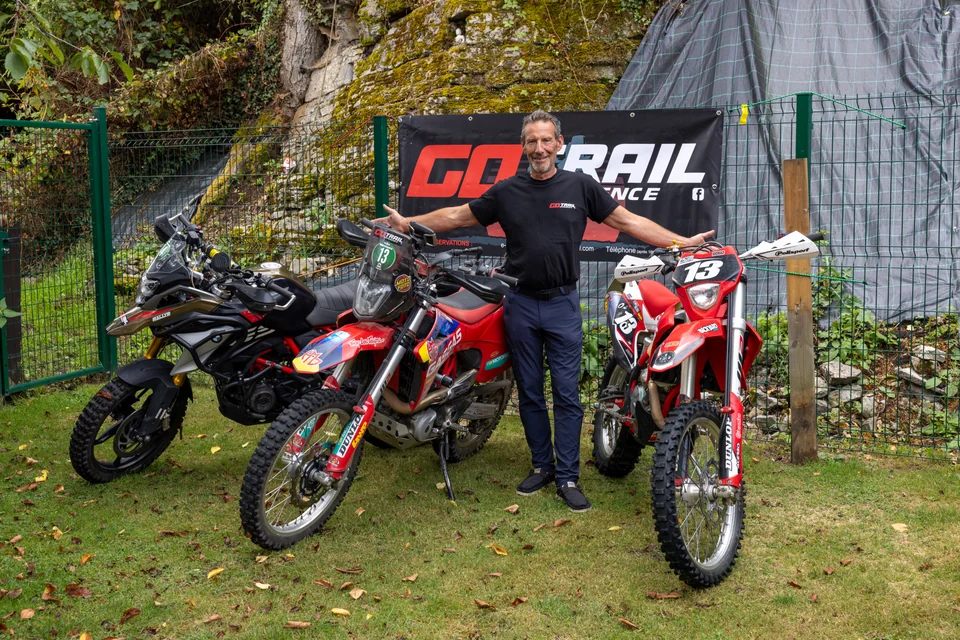Olivier pose dehors entre trois motos, devant une banderole Go Trail Experience.