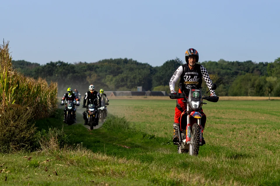 Olivier roule sur sa moto rouge le long d’un chemin herbeux, suivi du groupe.