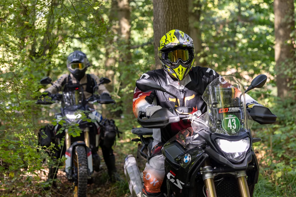 Un pilote sur BMW F900 ouvre le cadre, suivi d’autres motos entre les arbres.