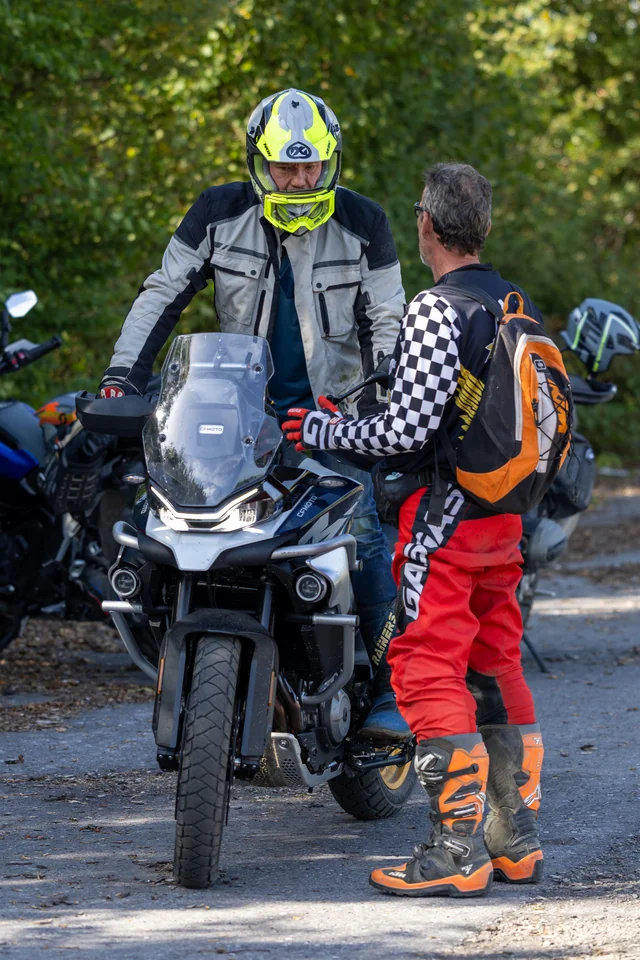 Olivier parle avec un pilote au casque jaune, assis sur un trail.