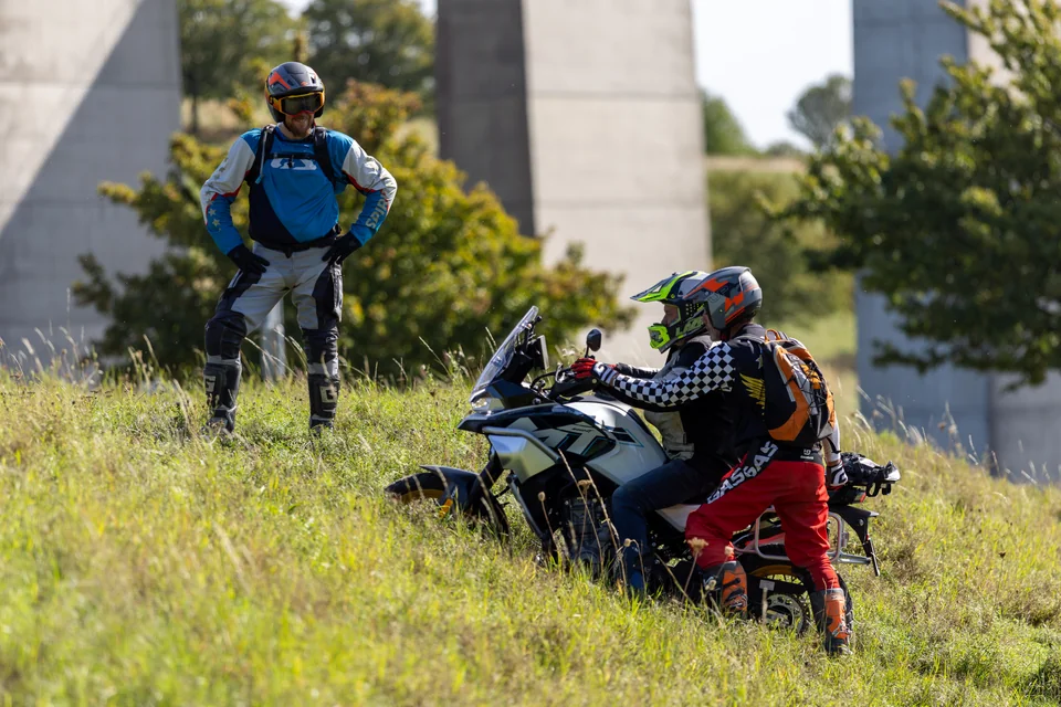 Olivier, assis sur une moto, échange avec un pilote debout dans l’herbe.
