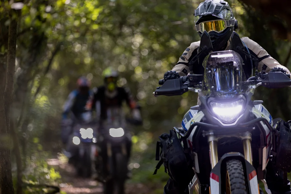 Un pilote au casque jaune approche sur un trail, avec d’autres pilotes derrière lui.