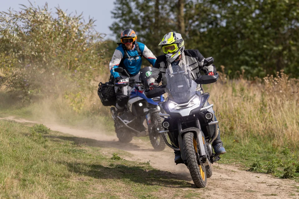 Deux pilotes suivent un chemin sec, avec de la poussière derrière leurs motos.