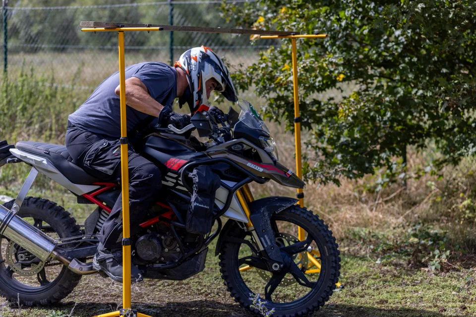 Un pilote se penche sur sa moto pour passer sous une barre horizontale jaune.